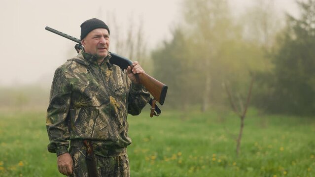 Morning foggy hunting on the background of autumn field. The hunter, armed with a rifle and a knife, saw the prey. He puts down his weapon, puts on tears and aims