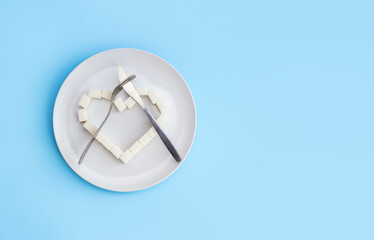 Heart made of sugar cubes on plate and crossed fork and knife. Refusal of unhealthy food. Danger of obesity or diabetes. Sugarfree concept. Selective focus, copy space