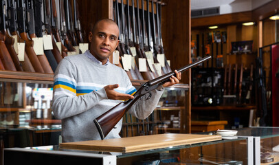 Confident latin american man owner of armory shop standing behind counter and offering vintage...
