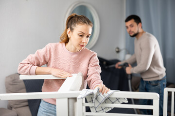 Portrait of young woman keeping home clean together with her husband polishing wooden furniture and doing vacuuming