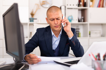 Focused man using laptop and talking by phone at the office table