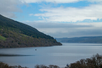 Obraz premium Scenic landscape view of Loch Ness in Scotland with the Scottish highlands and blue sky background, and brush vegetation in the foreground