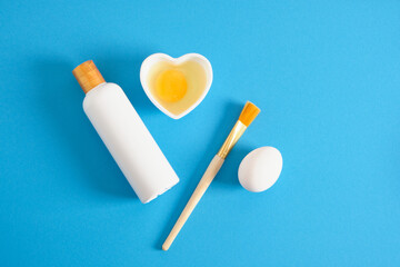 mock up white cosmetic bottle and heart shapes bowl with raw egg and cosmetic brush, face mask with eggs