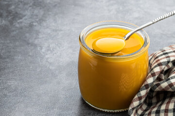 Yellow and orange fruit puree in glass jar on gray background