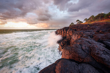 Stormy clouds at sunrise and crashing wave on cliffs, Giant's Causeway, Fingal Head, NSW, Australia