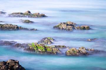 Serene seascape with long-exposure blue ocean water and moss-covered coastal rocks