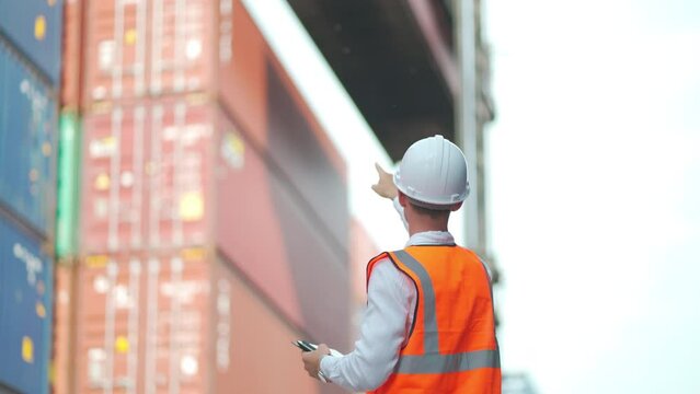 Cargo Container Worker Hold Tablet And Look Like Control Crane Lifting Up The Tank Then Turn Back And Look At Camera With Smiling.