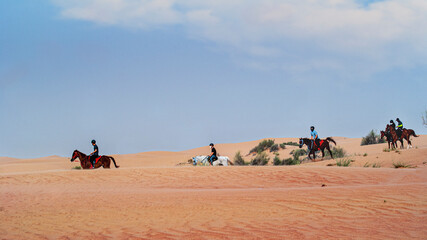 Fototapeta na wymiar Horseback riding in the desert. Beautiful wavy sands, dunes and riders on horseback.