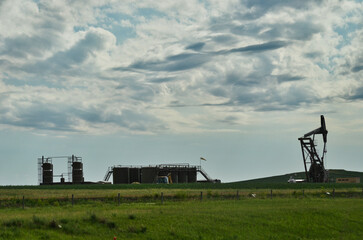 View of Drilling Rig and Tanks in Meadow under Cloudy Skies 