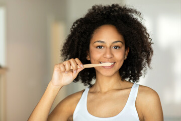 Happy black woman brushing her teeth with a toothbrush, looking at the camera