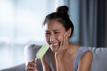 Young Asian woman have sensitive teeth with ice. Feman eating ice cream have toothache. Healthcare concept.