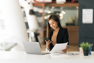 Fototapeta premium Asian woman using smart phone and laptop in modern office.