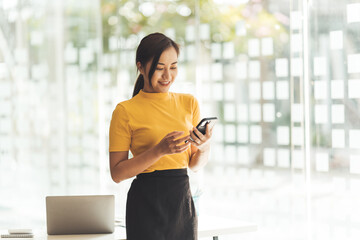 Smiling businesswoman using phone in office. Small business entrepreneur looking at her mobile phone and smiling, Young businesswoman holding a smartphone in a co-working space.