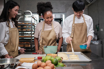 Cuisine course, a young male chef in apron and group of cooking class students, brushes pastry...