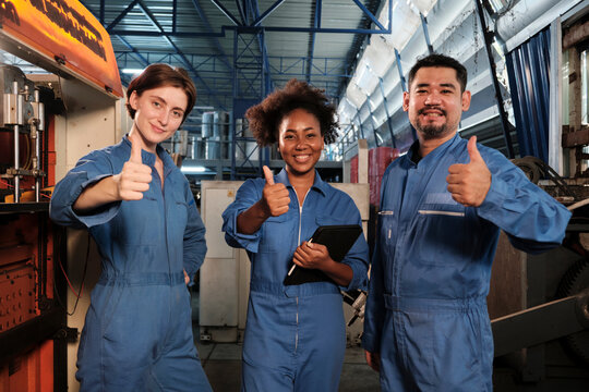 Cheerful multiracial industry workers in safety uniforms line up and thumb up together after work success and express smiles and happiness in mechanical factory. Professional engineer occupation.