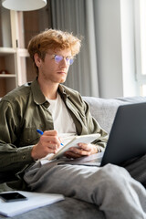 Focused young ginger man watching webinar using laptop to study online