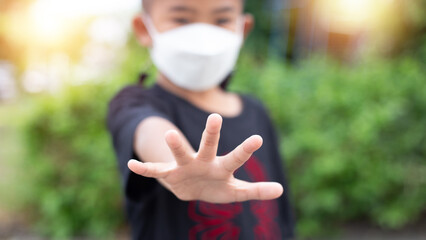 A 5 year old Asian boy wears a medicine healthcare mask and raises his hand. Do not approach. to maintain social distance To prevent the spread of the Coronavirus (Covid-19)