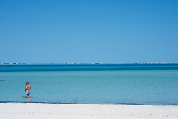 Rear view of a man standing on the beach in a bathing suit observing the horizon over the Caribbean Sea