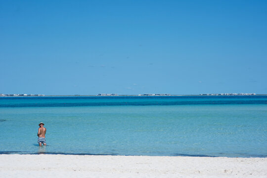 Rear view of a man standing on the beach in a bathing suit observing the horizon over the Caribbean Sea