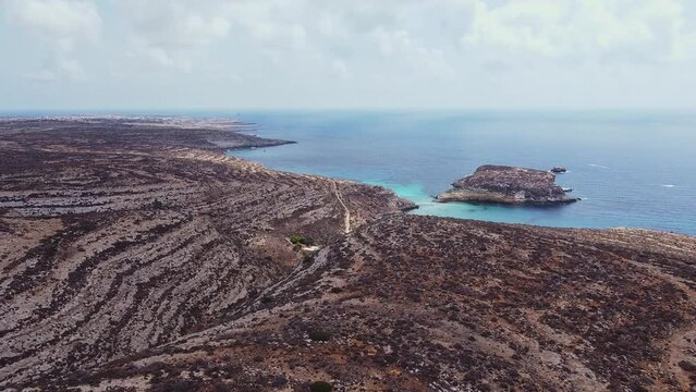 Aerial drone. Spiaggia and Isola dei Conigli, Lampedusa. Tranquil, cove-style beach with white sand and turquoise surf bordered by rocky cliffs.