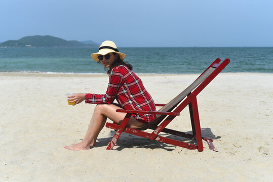 Young woman in hat sitting on the desk chair at the beach with white sand in Vietnam