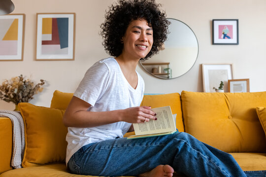 Portrait of smiling, happy young African American woman reading a book at home looking at camera.