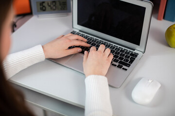 At her desk, a girl quickly types a message on her laptop keyboard.