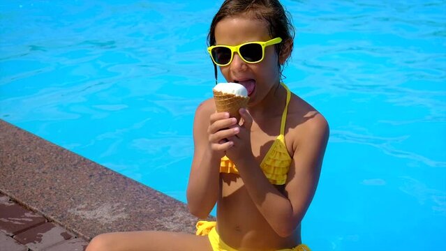 The child eats ice cream near the pool. Selective focus.