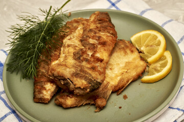 fried fish with lemon and herbs on a plate on the table