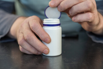 An adult man holds a white vial in his hands.