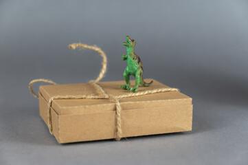 Brown cardboard box and a miniature dinosaur against a gray background. Small green figure of a...
