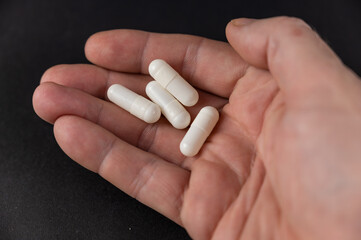A man is holding a white medicine pill. The medicine lies in the open palm of an adult's hand. Health and Medicine.