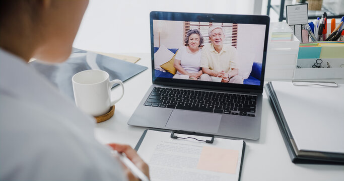 Young Asia Lady Doctor In White Medical Uniform With Stethoscope Using Computer Laptop Talking Video Conference Call With Patient At Desk In Health Clinic Or Hospital. Consulting And Therapy Concept.