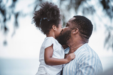 African American father carrying daughter and kisses on cheek with cheerful loving. Happy family.