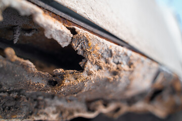 Rusted through the bottom of the door of a white car close-up