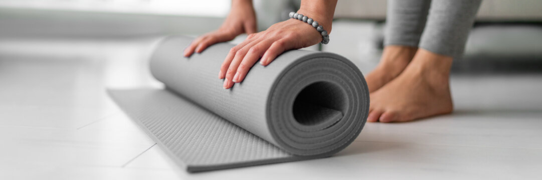 Yoga online class at home woman rolling mat on apartment floor for gym training or meditation banner panoramic. Feet and hands closeup