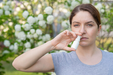 Caucasian woman uses a nasal spray while walking in the park. - obrazy, fototapety, plakaty