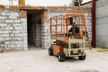 Fototapeta na wymiar Scissor Lift Platform on a construction site. Building concreate house with mobile transportation vehicles. Industrial machine for work on height