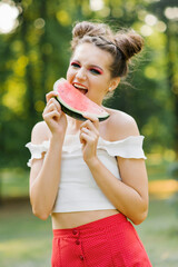 A smiling girl holds a sweet watermelon in her hands and smiles while biting it