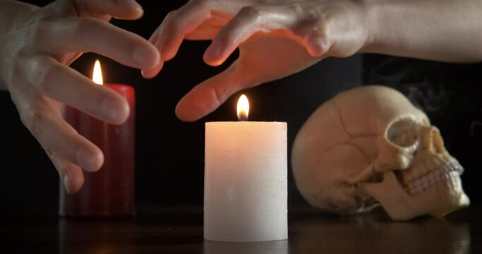 Black magic. Female hands conjure over a burning candle on the background of a human skull.