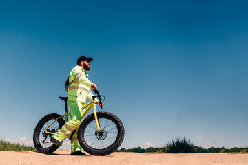 Naklejka premium Fat-tire bike in summer driving through the hills. Man is posing with a fat bike in the forest. He performs some tricks and runs dangerously. Bicycle with thick wheels in nature.