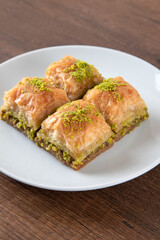 Pistachio baklava in a white plate on wooden background	