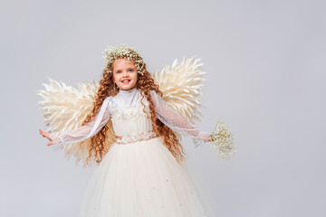 Fototapeta na wymiar charming little girl with curly hair, dressed in an angel costume with big wings and flower crown. She holds bouquet gypsophila flowers in her hands. Posing in the studio on white background.