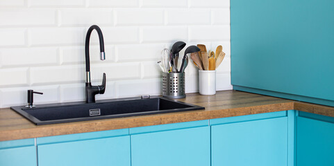 Black sink and faucet in blue kitchen with white backsplash and wood countertop