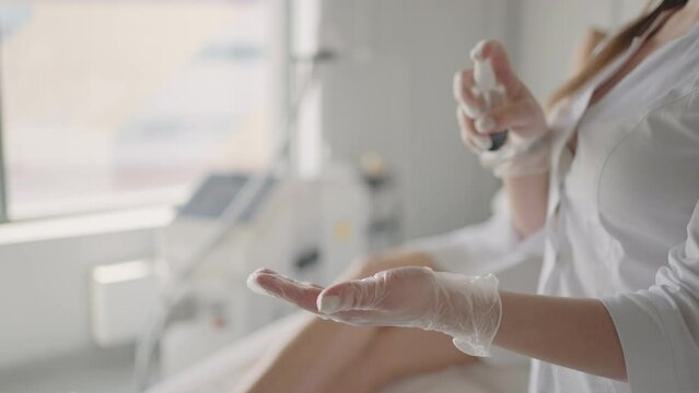 cosmetologist or physician therapist woman is spraying disinfectant on hands in gloves before medical treatment