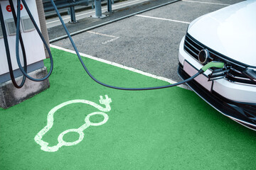 Electric car icon printed on green floor in electric vehicle charging station with car plugged on