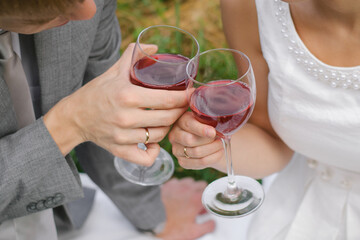 The bride and groom with wedding rings hold glasses of red wine in their hands