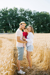 A young mother, father and little son enjoy nature together in the fresh air. A happy family with a child walks through a wheat field and enjoys the sweet moments of their life