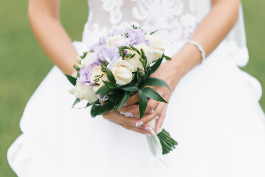 The bride's wedding bouquet of milk roses and lilac eustoms in the hands of the bride