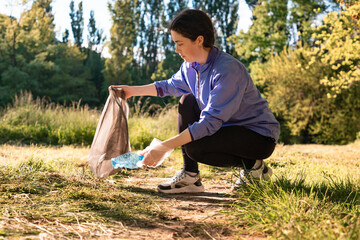 Young woman in sportswear picking up plastic bottles and put into garbage bag. Side view. The...